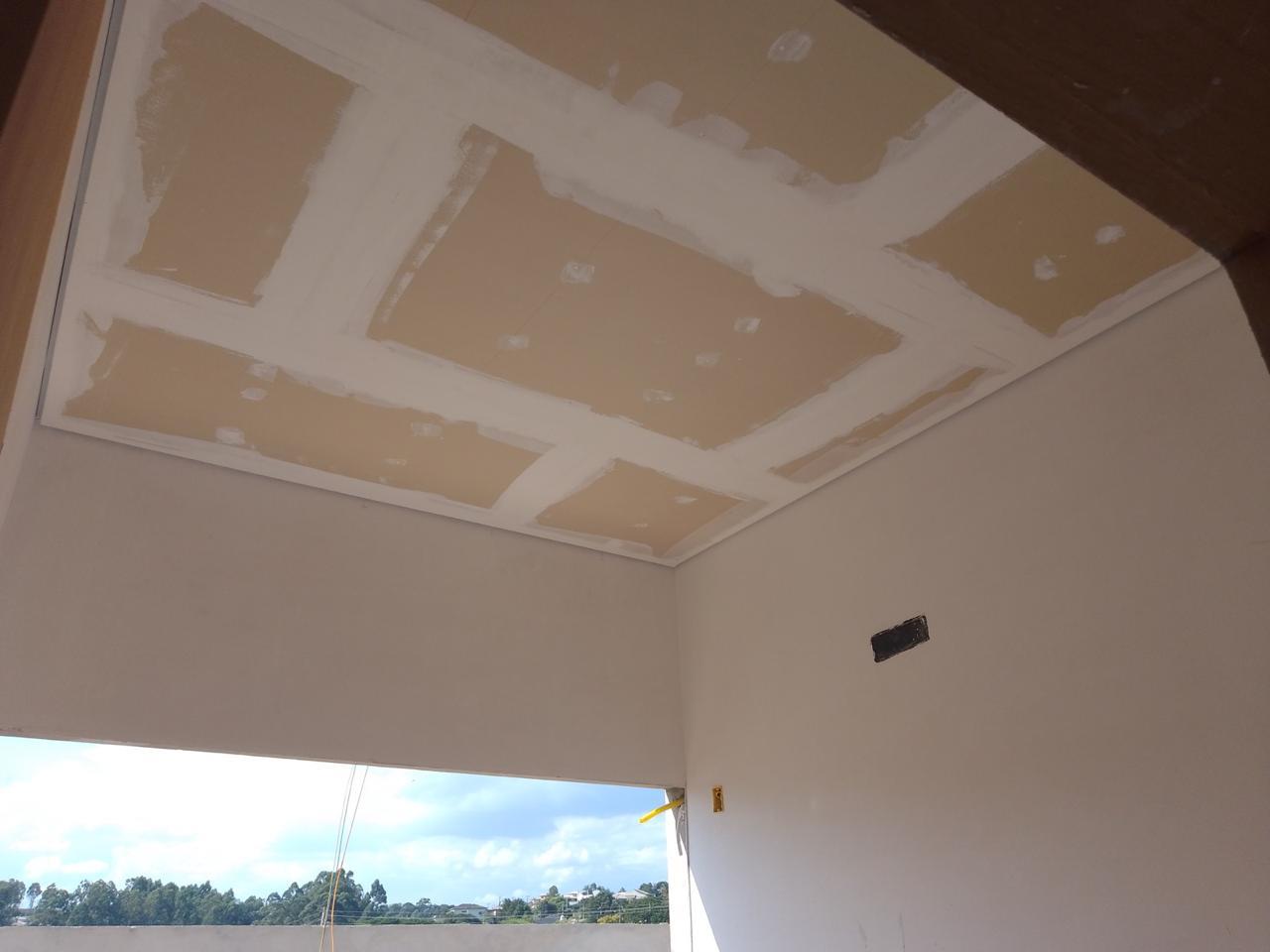 interior de uma sala em construção com teto de gesso e janelas abertas para o exterior  — texto:  
