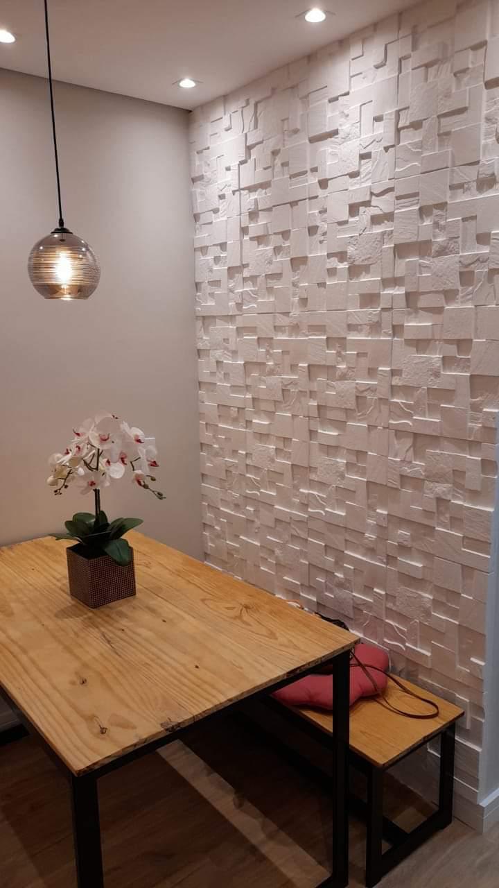 um ambiente interior com mesa de madeira, orquídea, luz pendente e parede texturizada em branco  — texto:  