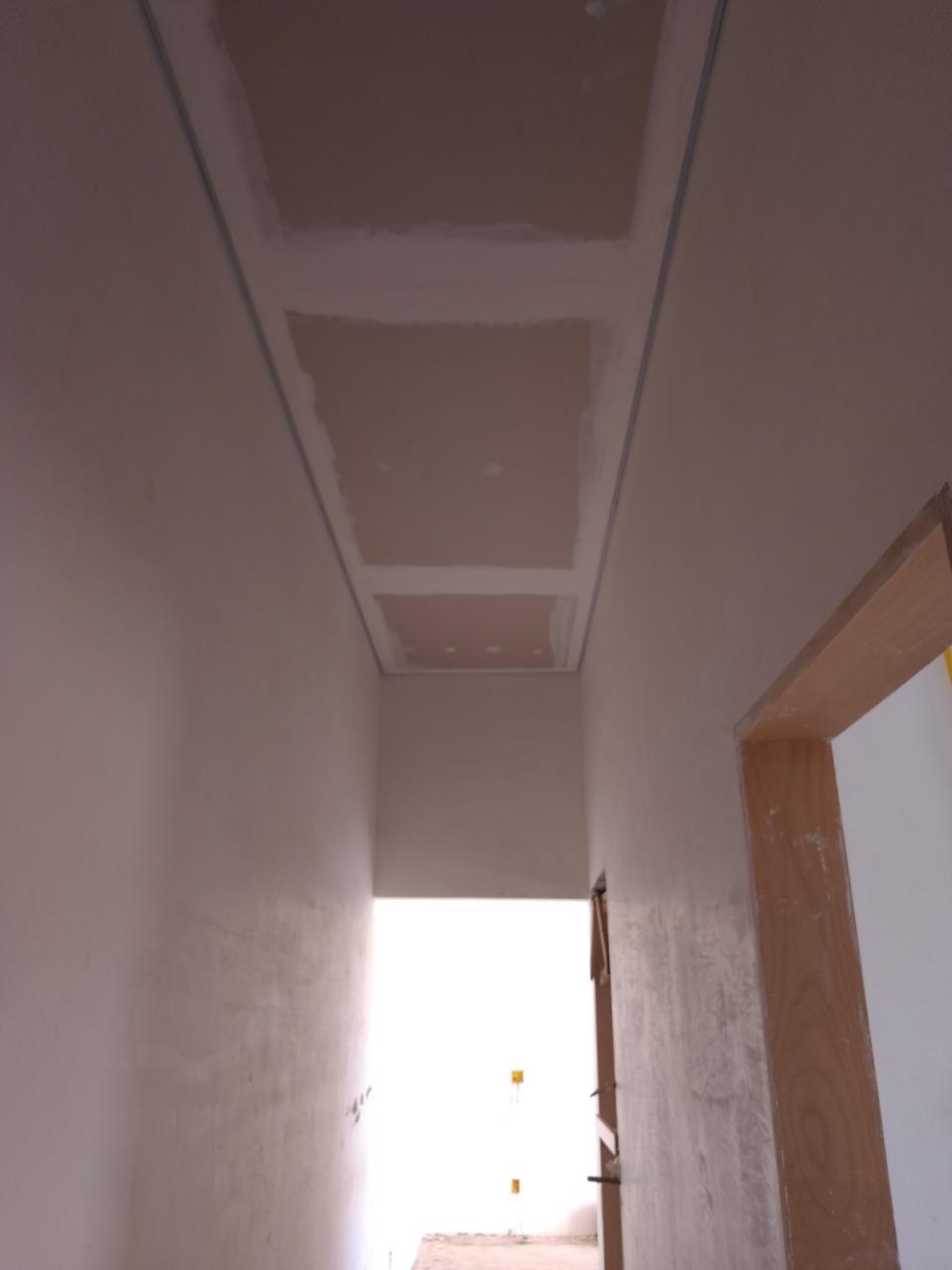 uma foto interna de uma sala em construção, com gesso no teto e paredes brancas, uma porta de madeira aberta p
