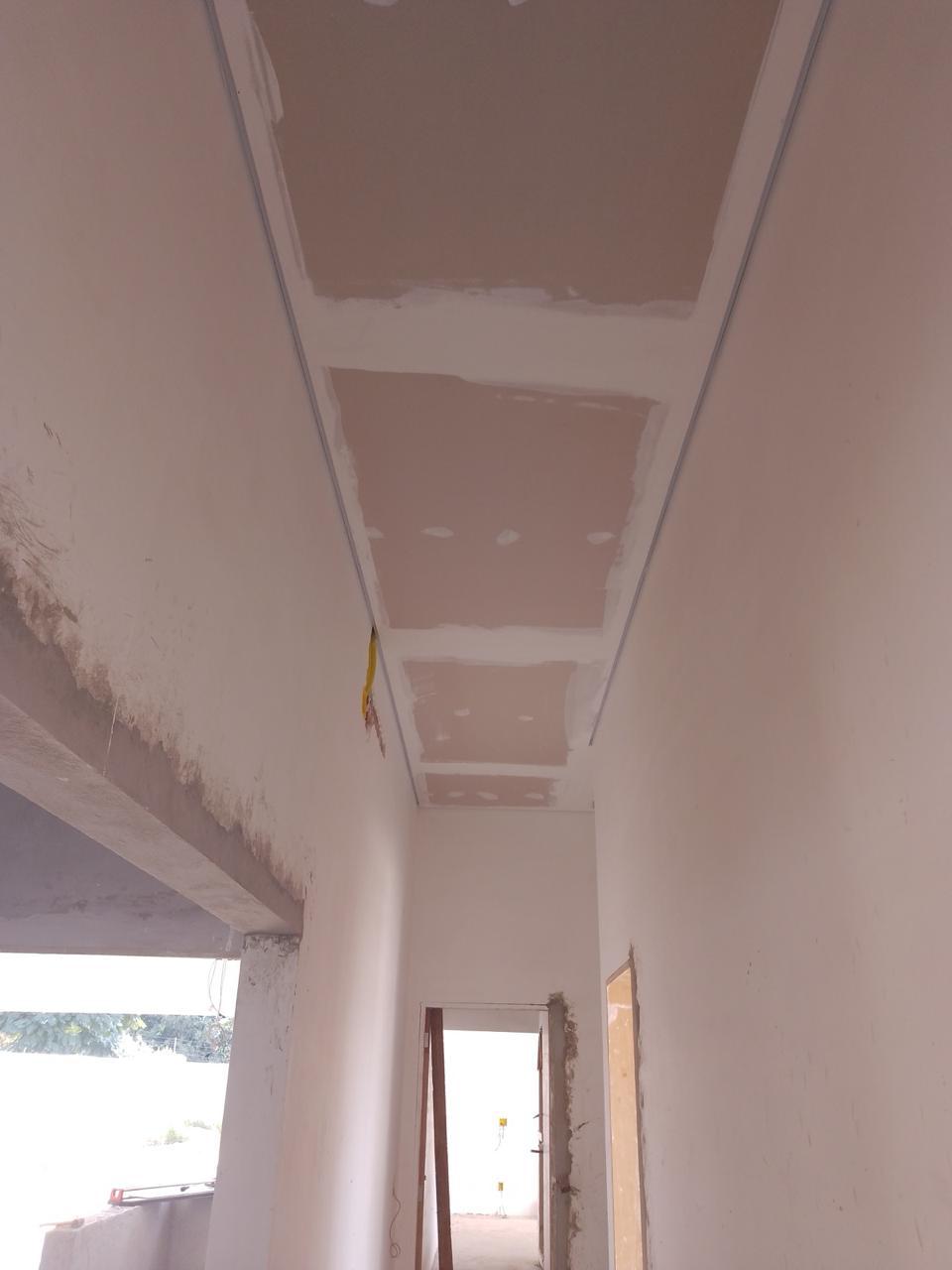 interior de uma construção em andamento com gesso em placa no teto e paredes brancas, com uma janela e portas 