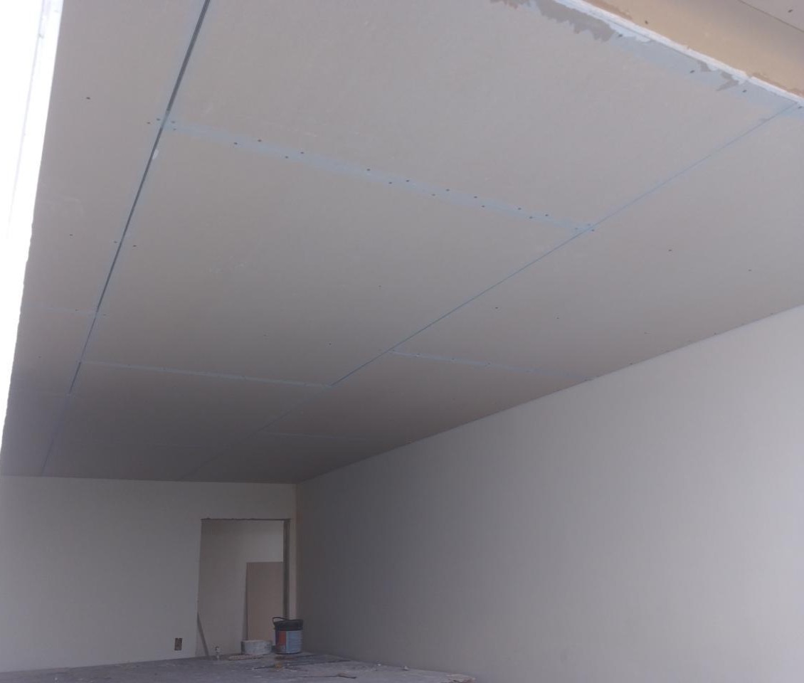 interior de uma sala em construção com teto em gesso, paredes brancas e um recipiente de tinta no chão  — text
